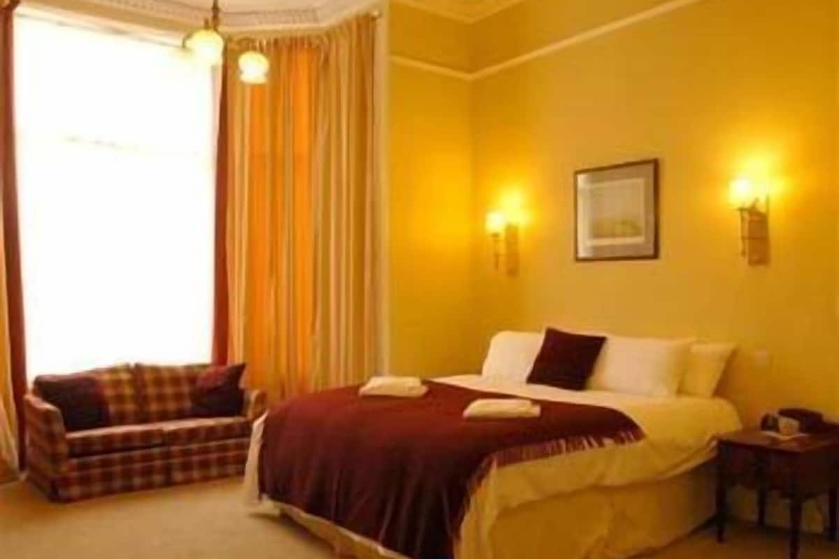 A hotel room with a bed, a chair, a nightstand, and a window with curtains.