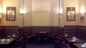 A formal dining room with high-backed booths, rectangular tables, and wall-mounted light fixtures. - The Guards Hotel (Edinburgh)