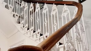 A wooden spiral staircase with ornate white railings and a patterned sofa in the foreground. - The Guards Hotel (Edinburgh)