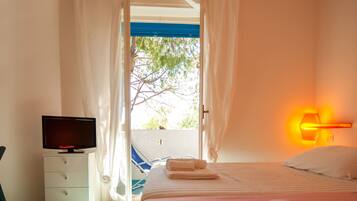A hotel room with a bed, a TV, a nightstand, and a view of the outdoors.