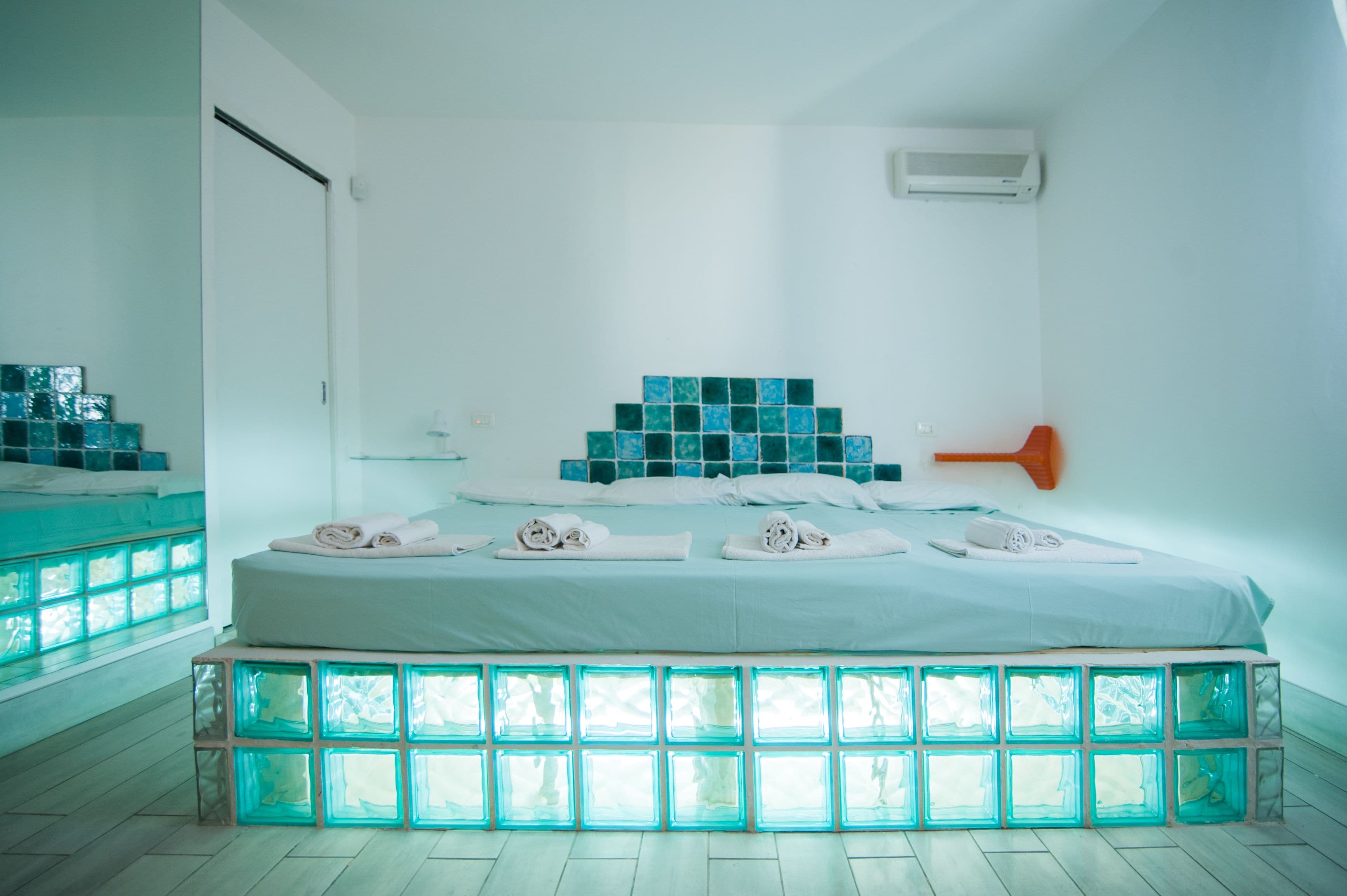 Un dormitorio moderno con cama, un banco de vidrio y un aire acondicionado de pared.