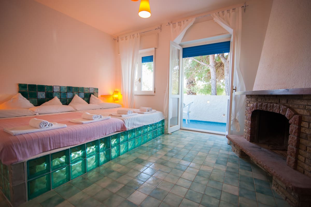 Ein Schlafzimmer mit Bett, Kamin und Blick ins Freie.