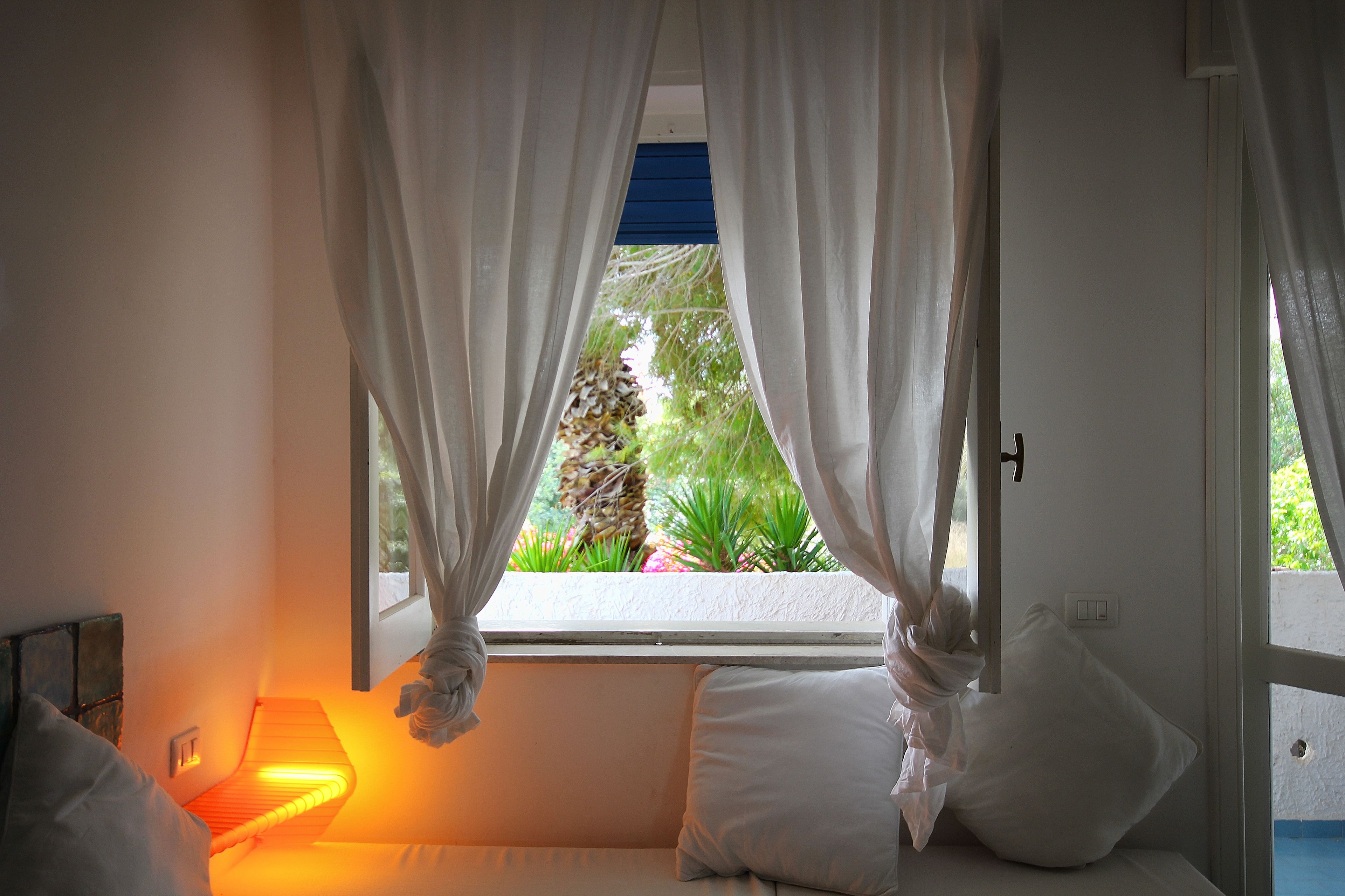 Ein Schlafzimmer mit einem Bett, einer Nachttischlampe und einem Fenster mit Vorhängen.