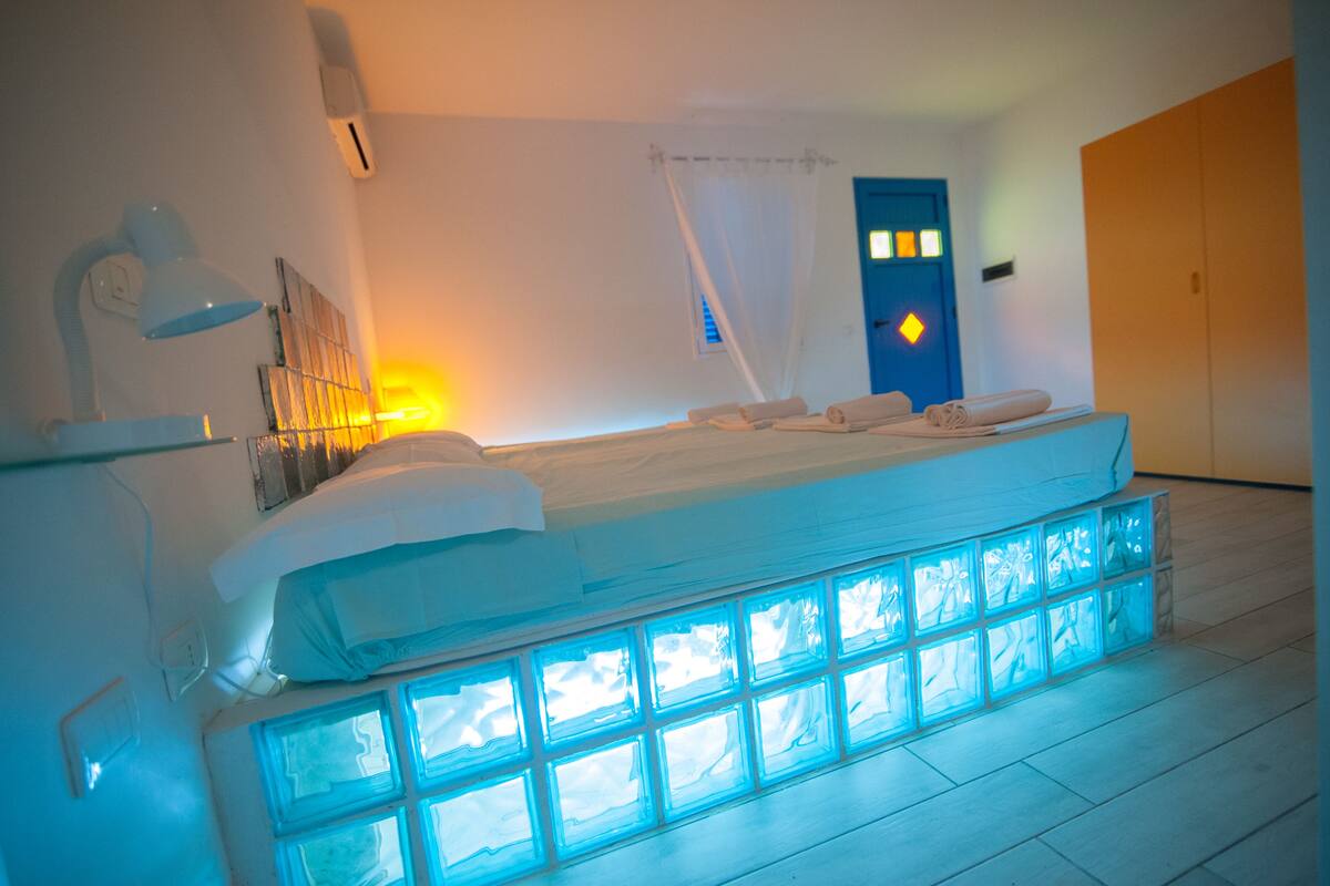 Ein Schlafzimmer mit einem Bett, einem Nachttisch, einer Lampe, einem Fenster mit Vorhängen und einer Tür.