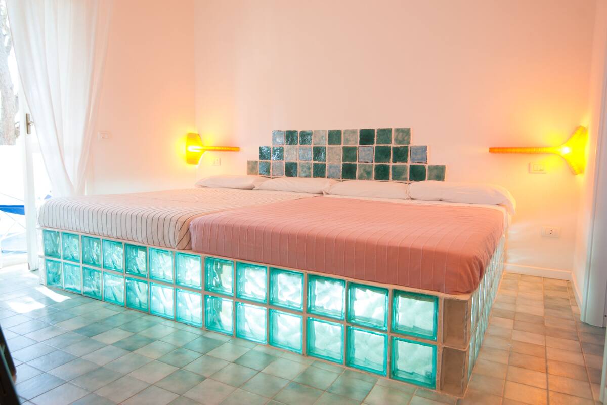 Ein Schlafzimmer mit einem Bett, weißen Vorhängen, Fliesenboden und Wandleuchten.