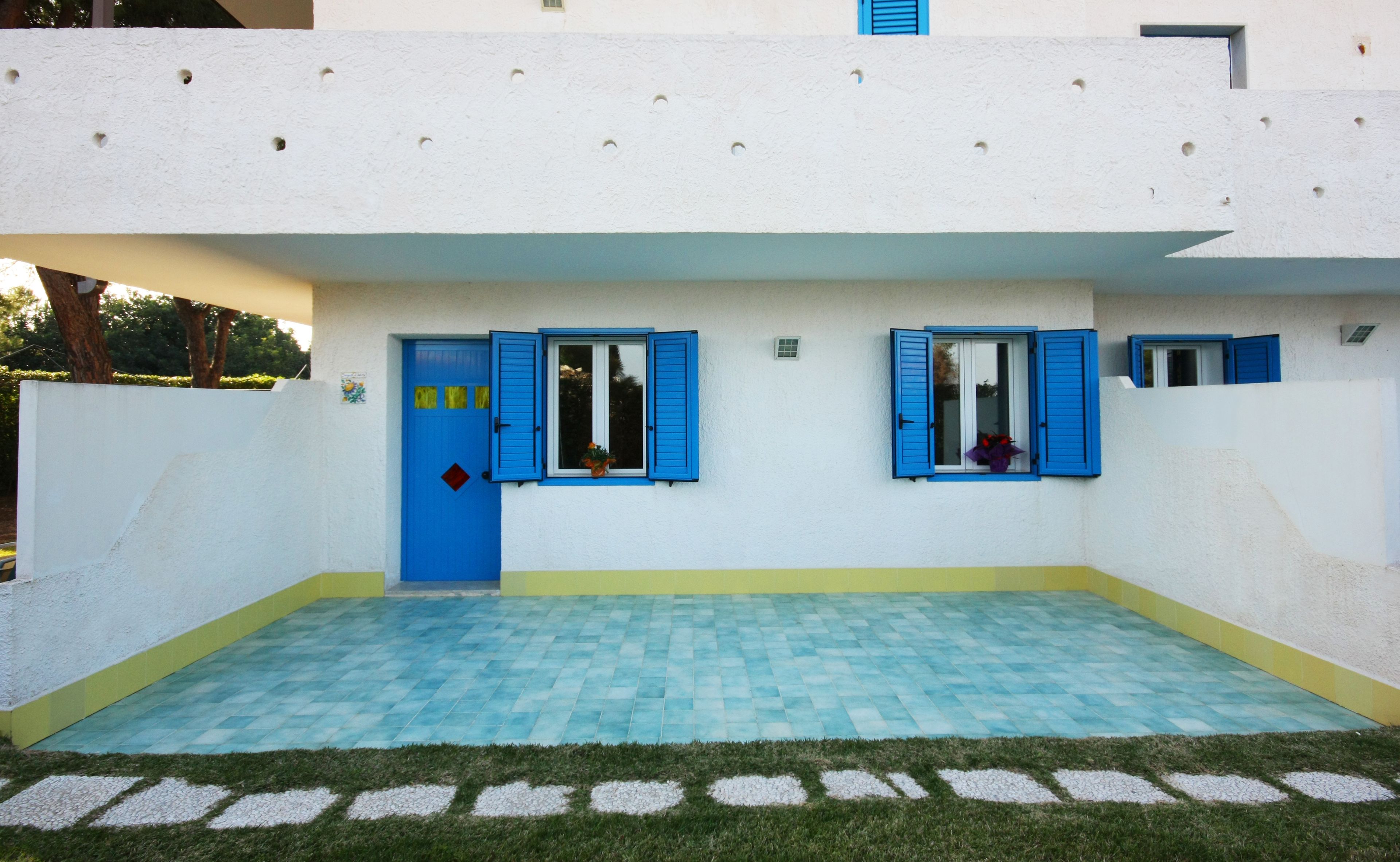 Ein Gebäude mit blauer Tür und Fensterläden, einem gefliesten Innenhof und einem grünen Rasen.