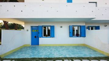 Ein Gebäude mit blauer Tür und Fensterläden, einem gefliesten Innenhof und einem grünen Rasen.