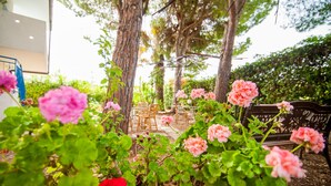 A garden area with pink flowers, a wooden bench, and a dining table set outdoors. - Suite House L'isola che non c'è (Syracuse)