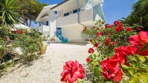 A modern white building with a unique architectural design, featuring a prominent staircase and a clear view of the surrounding garden with red flowers. - Suite House L'isola che non c'è (Syracuse)