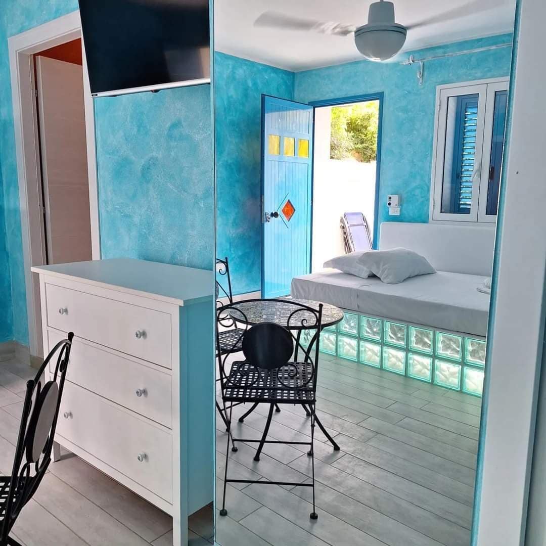Een kamer met een bed, een bureau en een stoel. Een deur leidt naar buiten.
