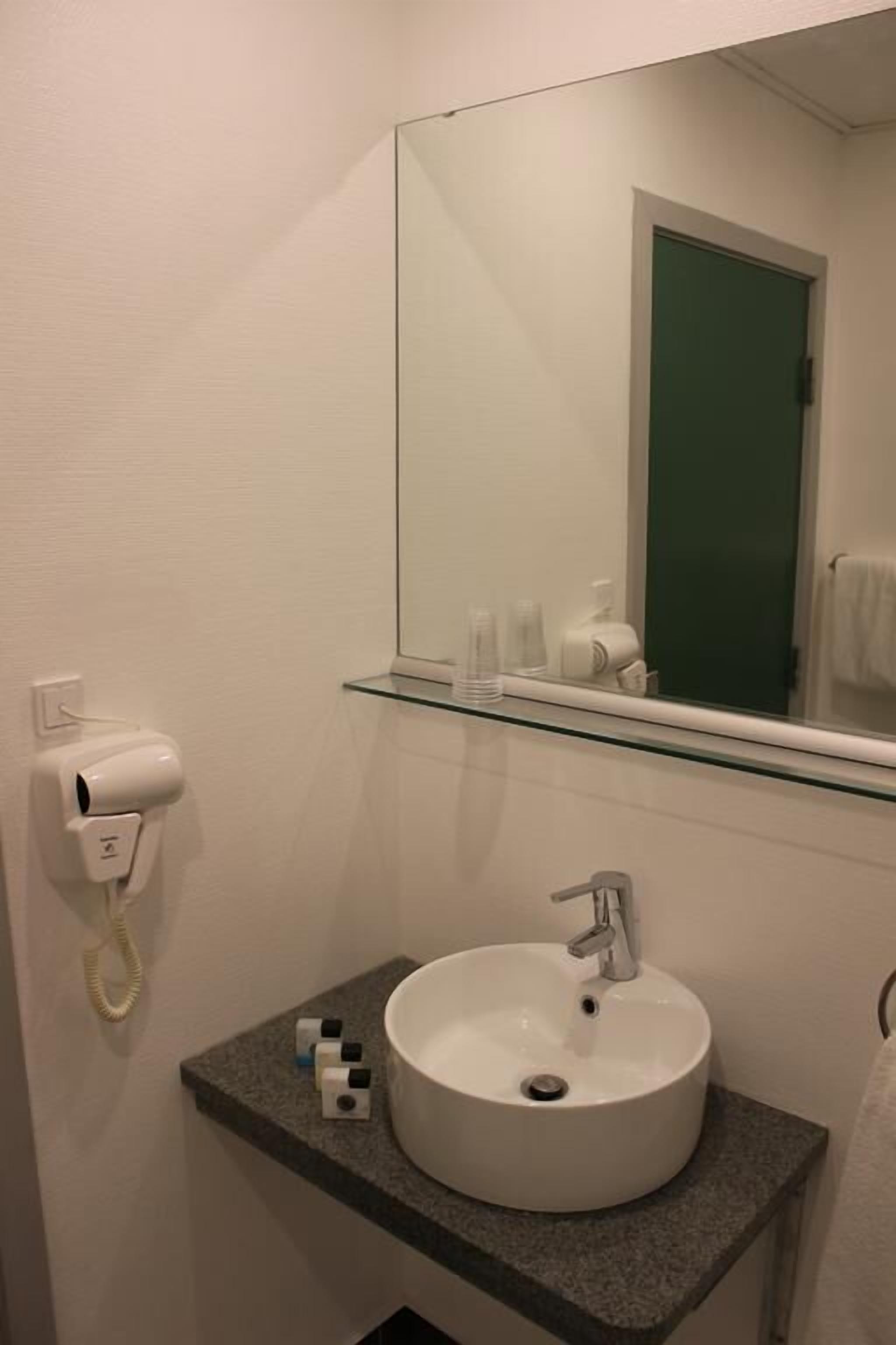 A bathroom with a white sink, a glass shelf, a mirror, and a towel rack.