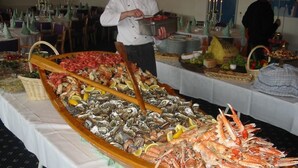 Una mesa de buffet con mariscos, incluyendo camarones y ostras, y un chef preparando comida al fondo.