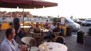 Un espacio de esparcimiento al aire libre con mesas redondas y sillas de mimbre, algunas con bebidas.
