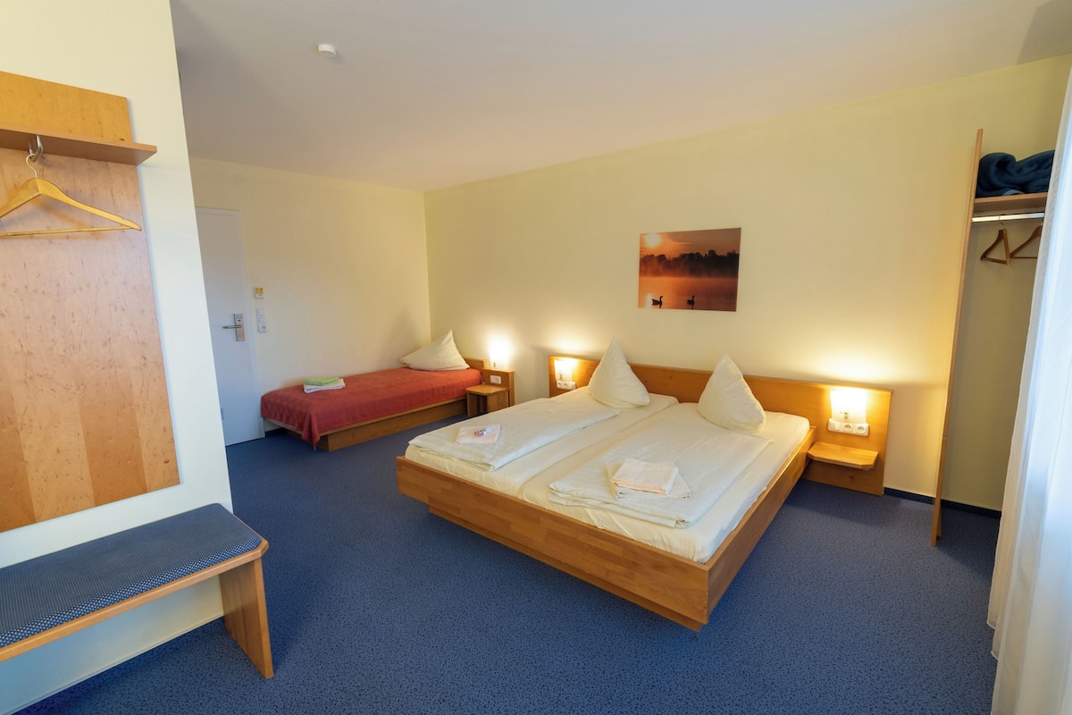 A hotel room with a large bed, a smaller bed, a bench, and a wardrobe.
