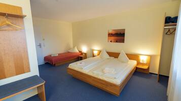 Une chambre d’hôtel avec un grand lit, un lit plus petit, un banc et une armoire.