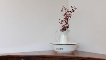 A white pitcher with red berries on a white bowl labeled "LE BAIN" on a wooden bench.