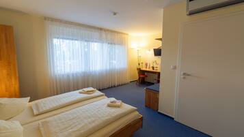 A hotel room with two beds, a desk, a chair, and a wardrobe.