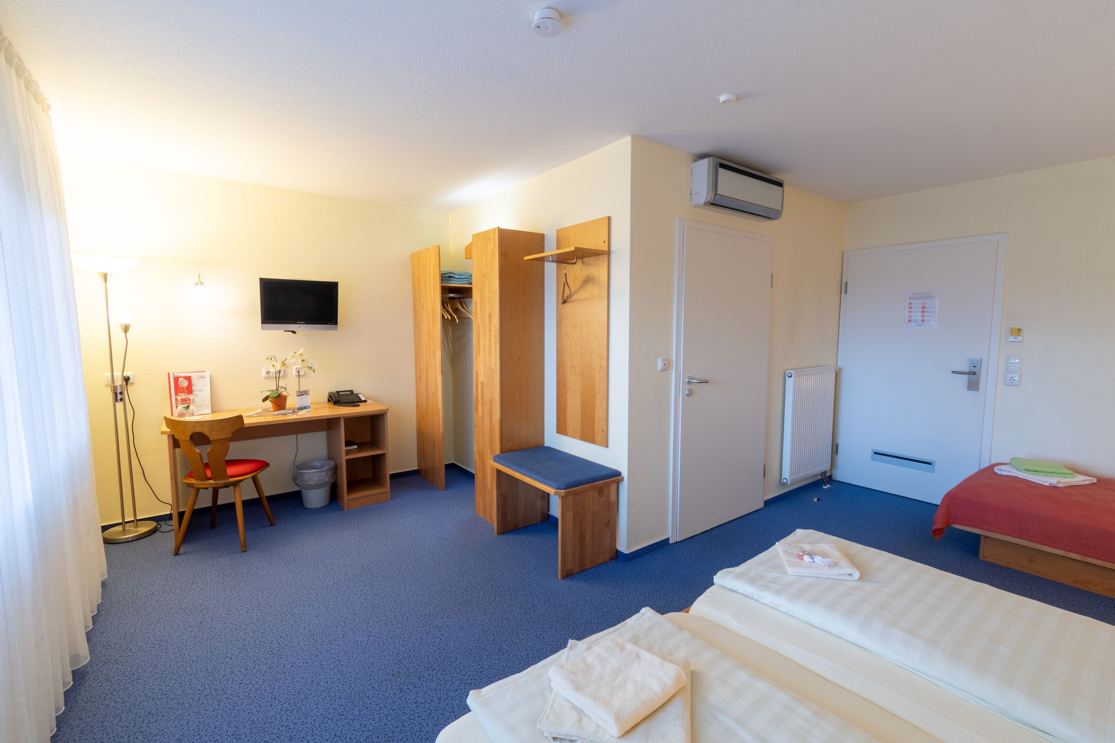 A hotel room with a desk, two beds, a wardrobe, a TV, and a radiator.