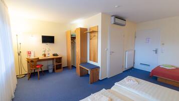 A hotel room with a desk, two beds, a wardrobe, a TV, and a radiator.