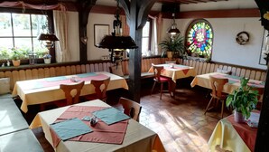 A cozy restaurant with wooden beams, multiple tables with tablecloths, and potted plants. - Hotel Landgasthof Ratz (Rheinau)
