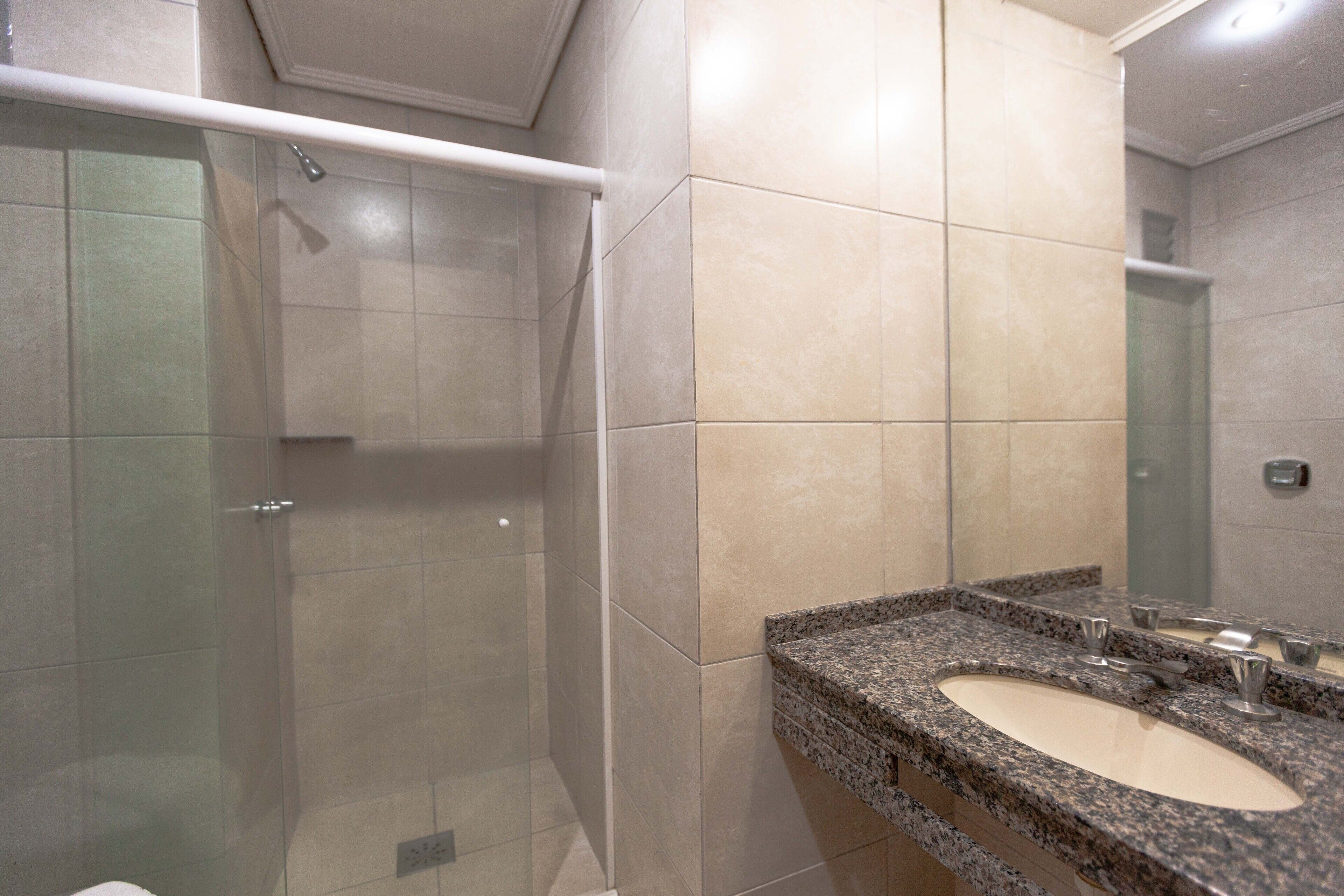A bathroom with a glass-enclosed shower, a granite countertop sink, and beige tiles.