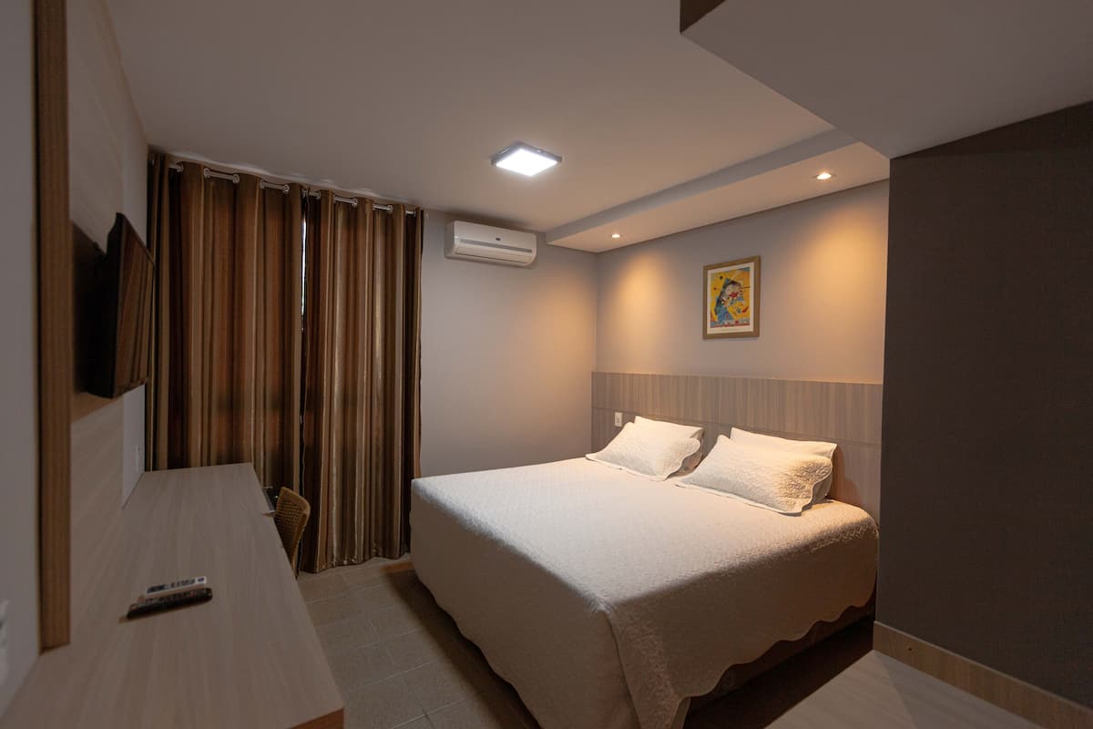 Un dormitorio con cama, escritorio, silla, televisor y aire acondicionado.