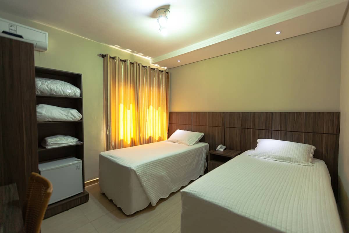 Una habitación de hotel con dos camas individuales, un armario, un escritorio pequeño y una mesita de noche.