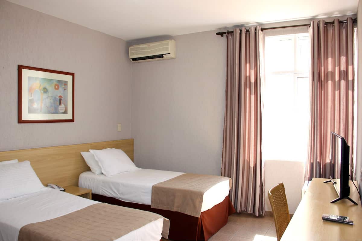Habitación de hotel con dos camas, un escritorio con televisor, una silla y un cuadro en la pared.