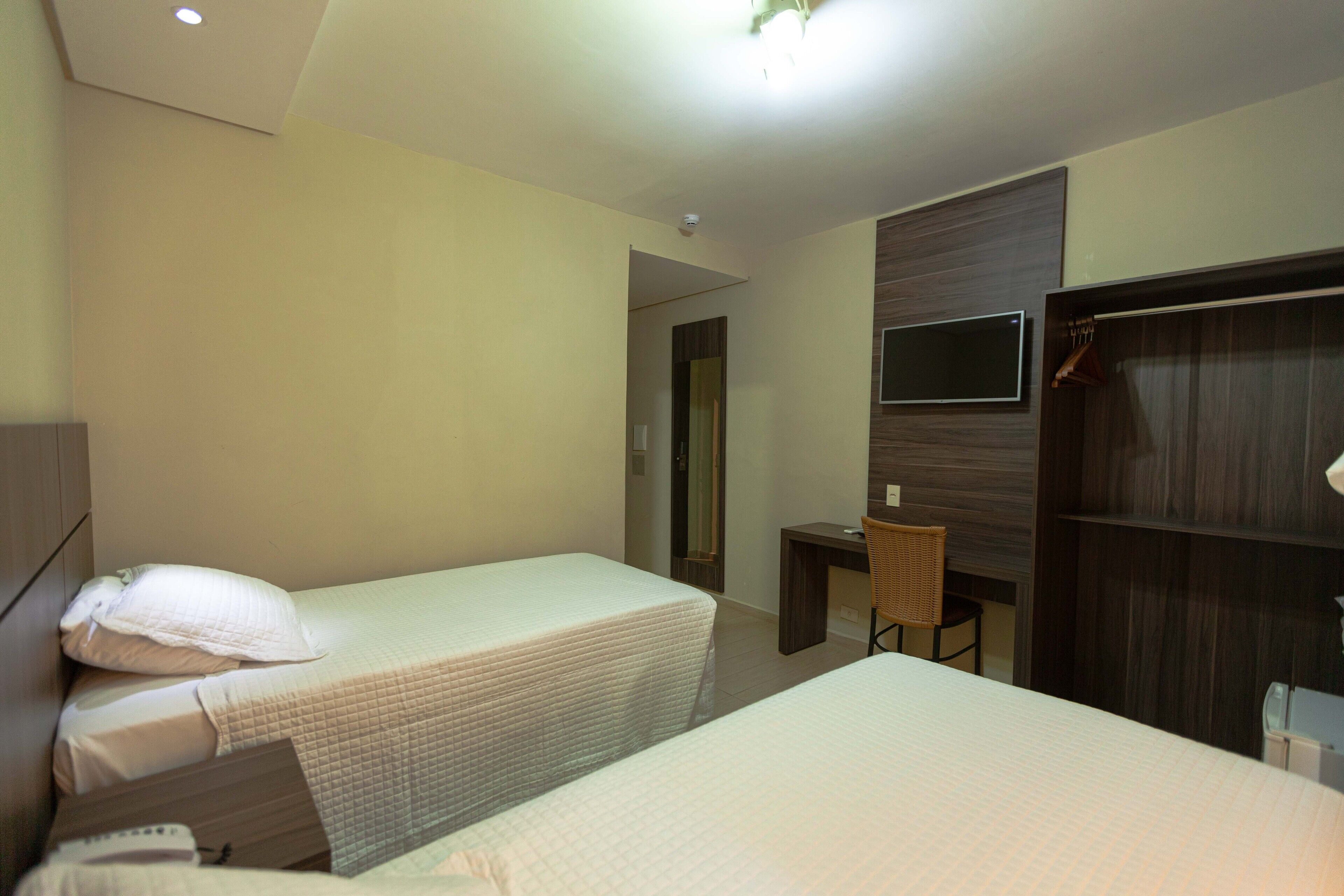A hotel room with two single beds, a desk, a chair, a wardrobe, and a television.