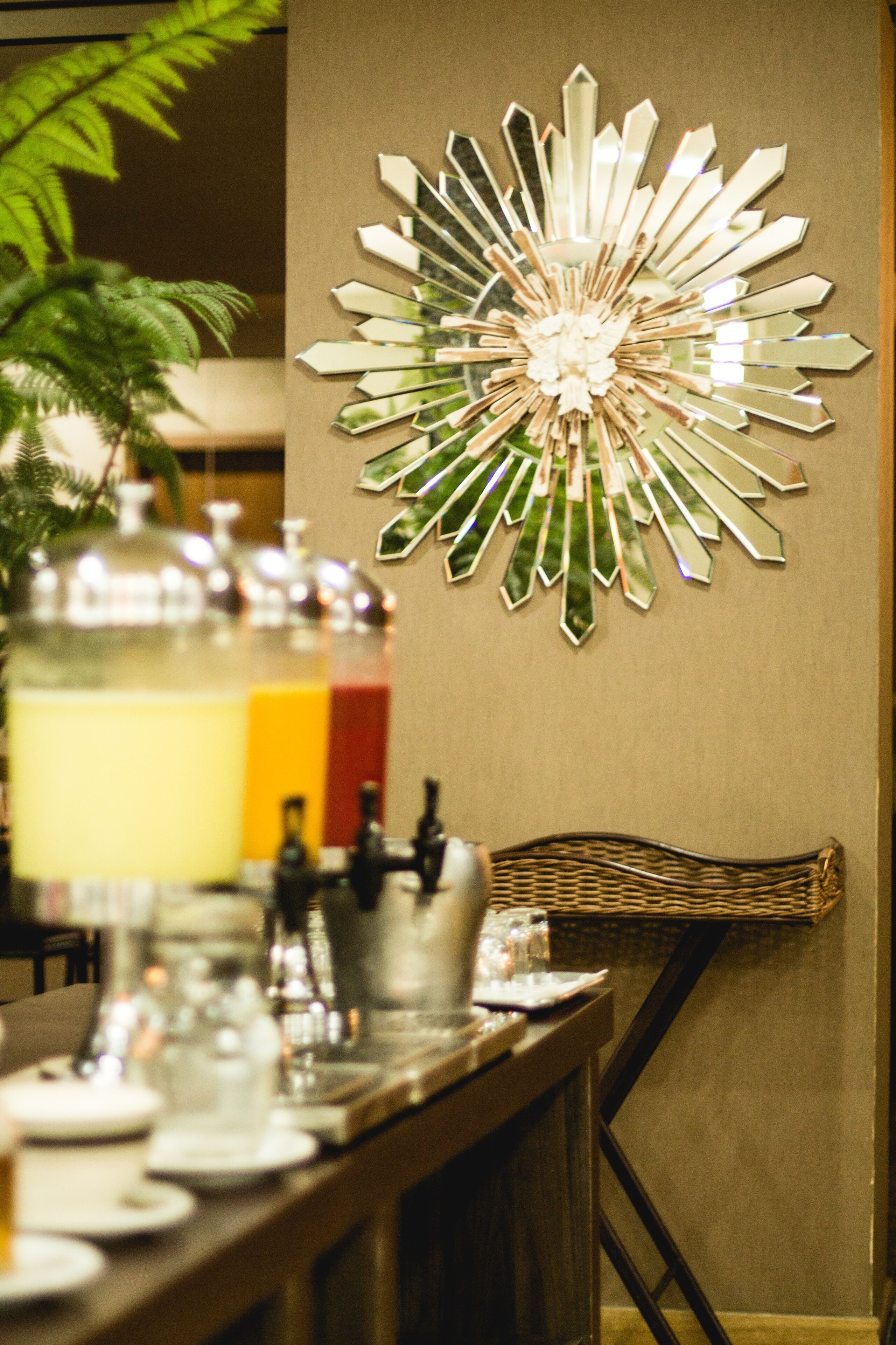 Un coin repas avec une longue table dressée pour le repas, un élément décoratif mural et une plante en pot.