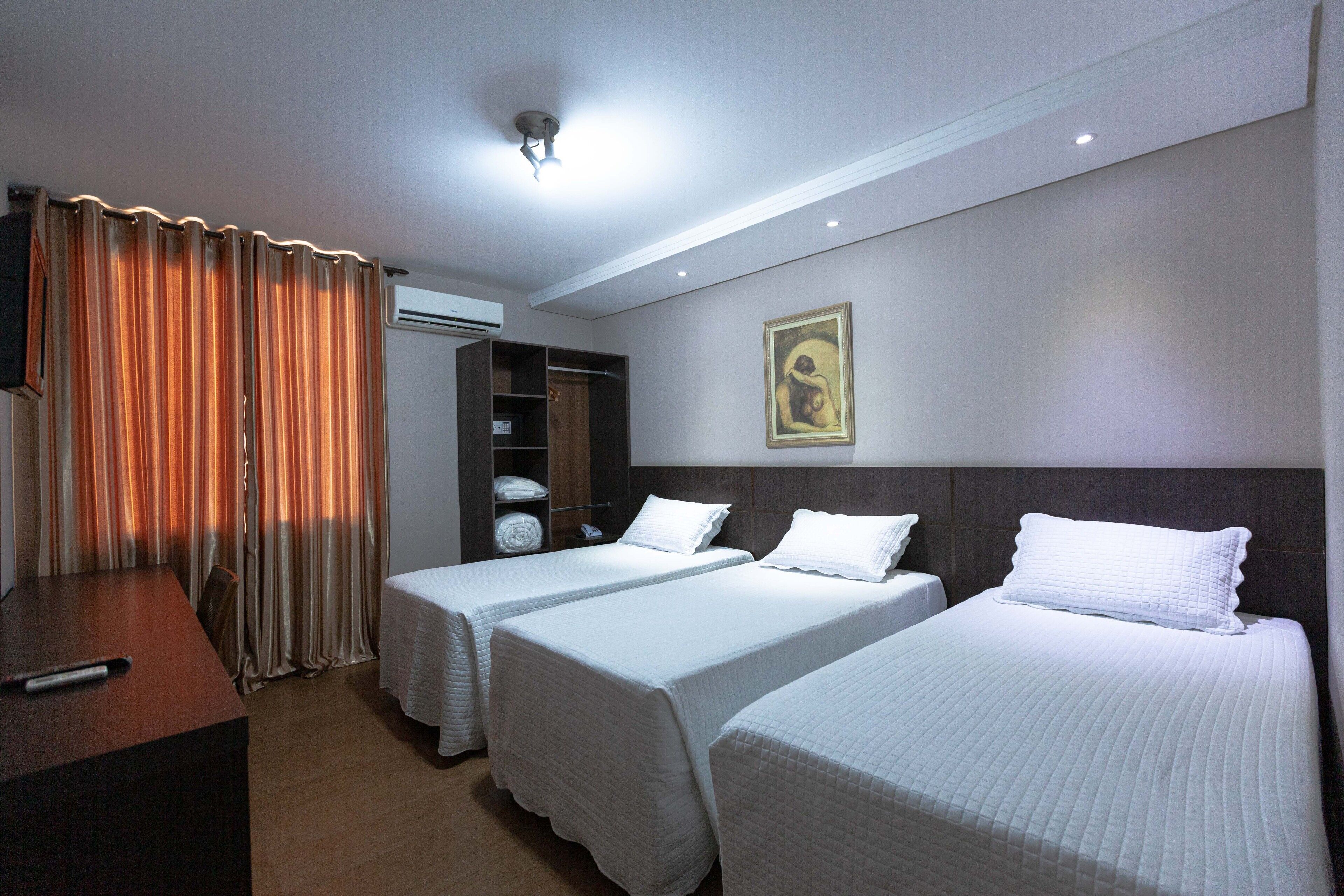 Habitación de hotel con dos camas individuales, un escritorio de madera, un armario y un cuadro en la pared.