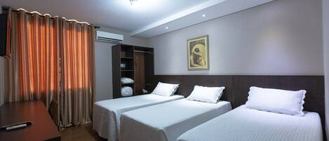 Habitación de hotel con dos camas individuales, un escritorio de madera, un armario y un cuadro en la pared.