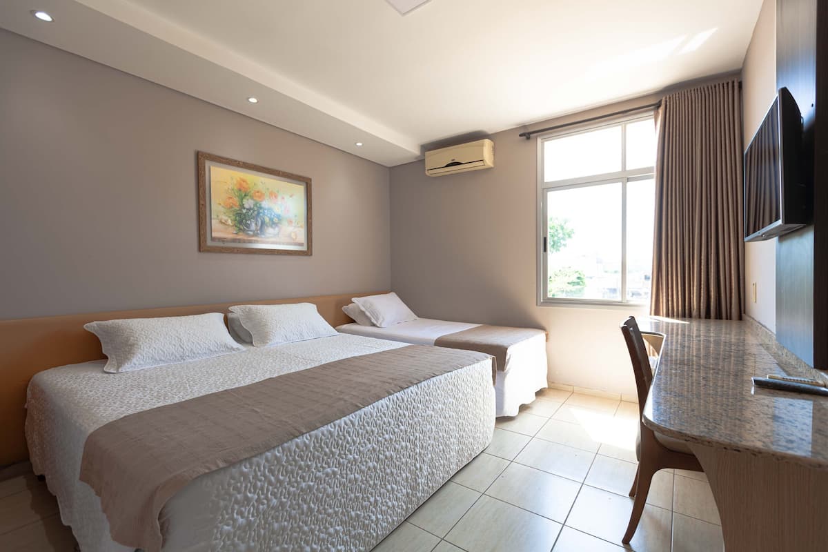 Habitación de hotel con dos camas, un escritorio, un televisor y una ventana con cortinas.