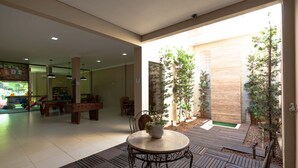 An indoor patio area with a round table and chairs, surrounded by potted plants and a wooden deck. - Hotel Foz do Iguaçu (Foz do Iguaçu)