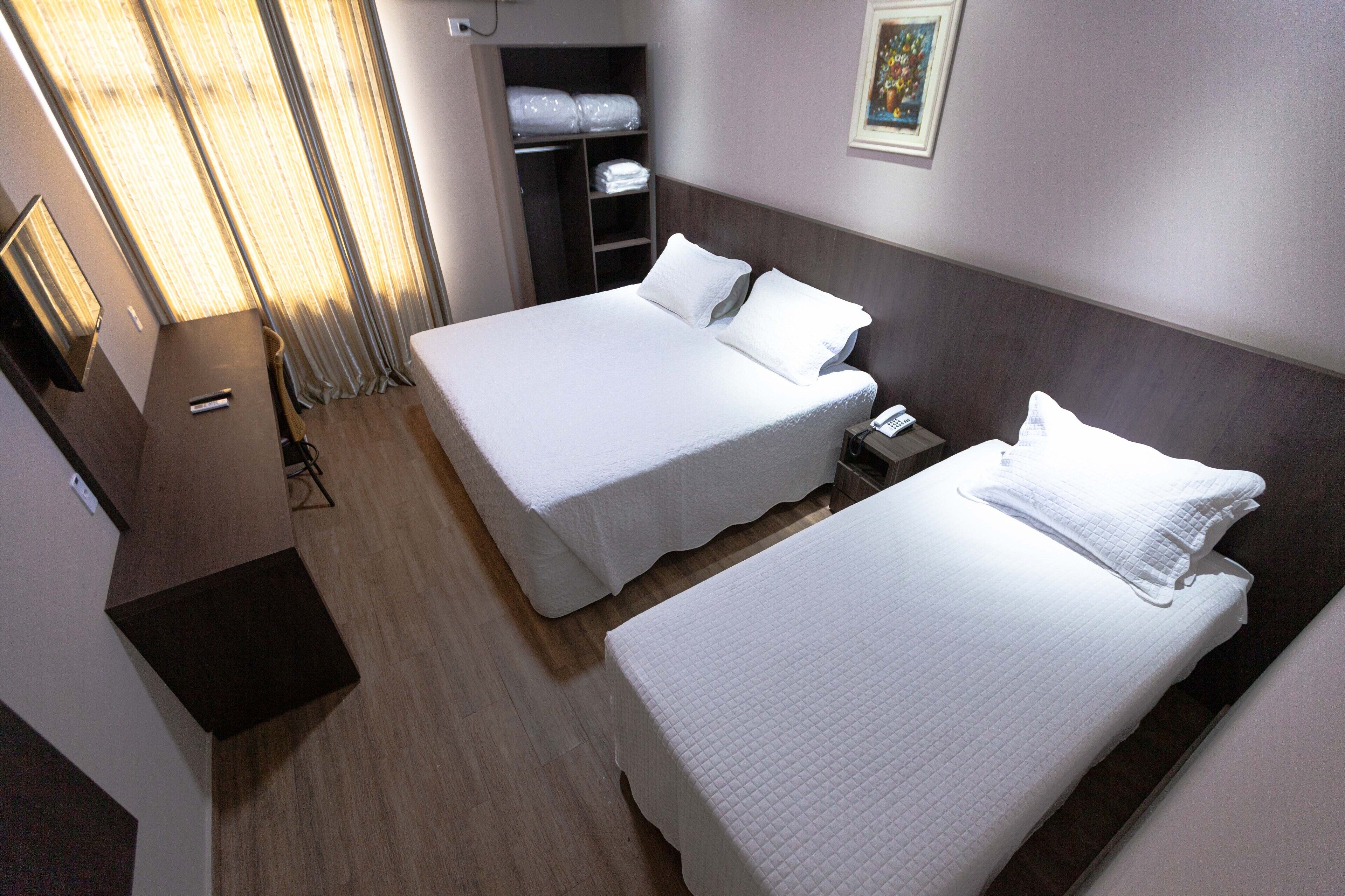 A hotel room with two beds, a bedside table with a phone, and a wardrobe with folded clothes.