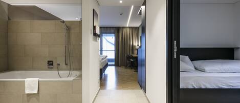 A modern hotel room with a separate shower area, a bed, a desk, and a view of the outdoors.