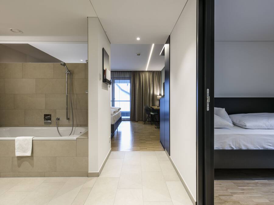 Ein modernes Hotelzimmer mit separater Dusche, einem Bett, einem Schreibtisch und Blick ins Freie.