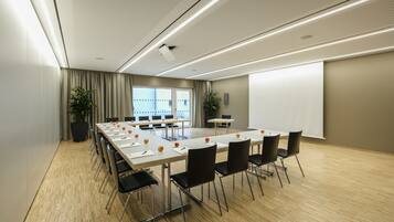 A conference room with a long table, black chairs, a projector screen, and a large window.