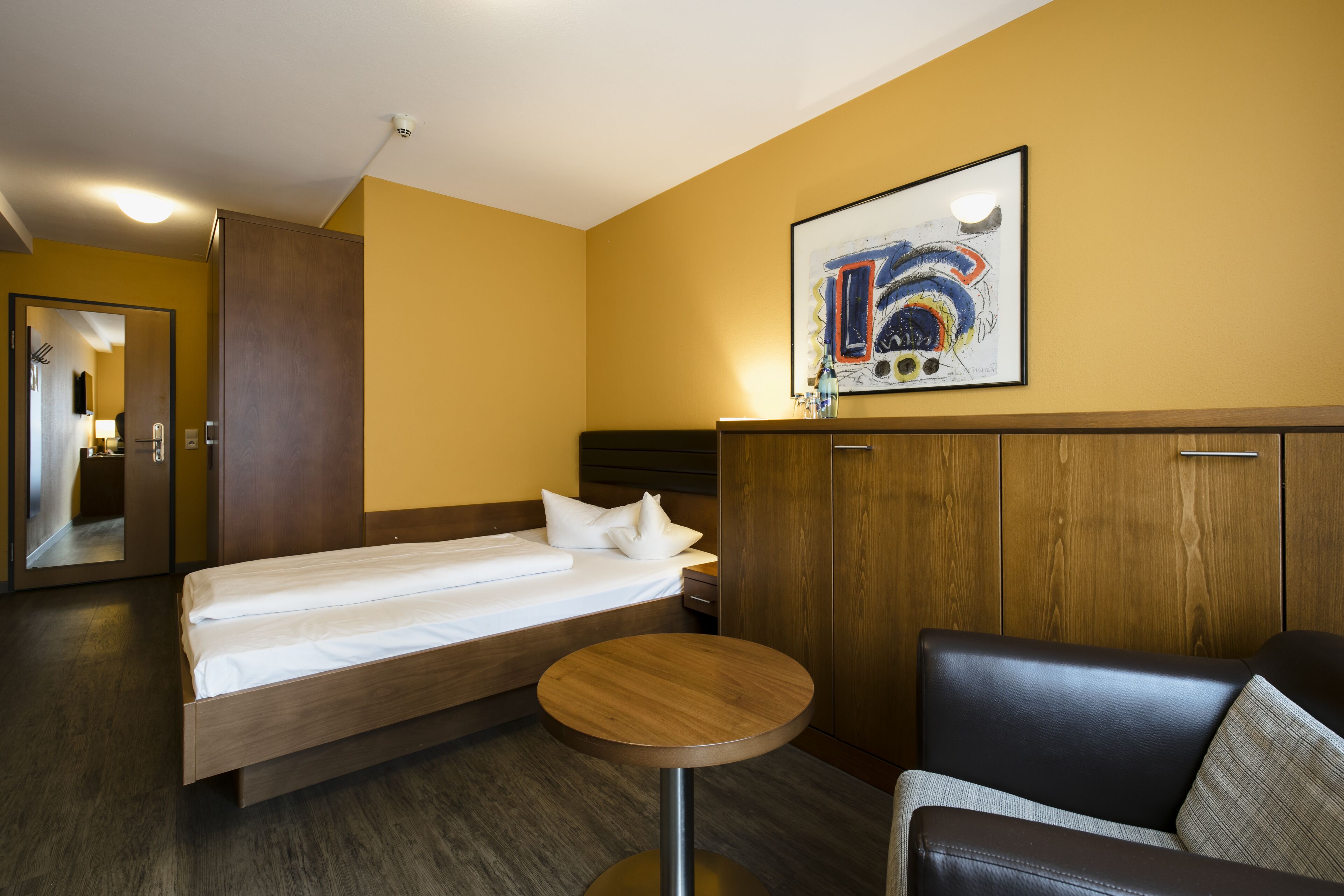 A hotel room with a bed, a round table, a couch, and a painting on the wall.