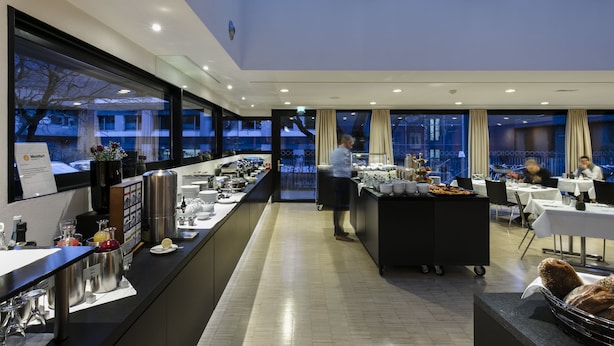 Ein modernes Hotelrestaurant mit einer langen Theke, Esstischen und einem Koch, der zubereitet.