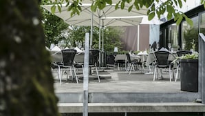 Ein Sitzbereich im Freien mit Tischen und Stühlen unter Sonnenschirmen, umgeben von viel Grün.