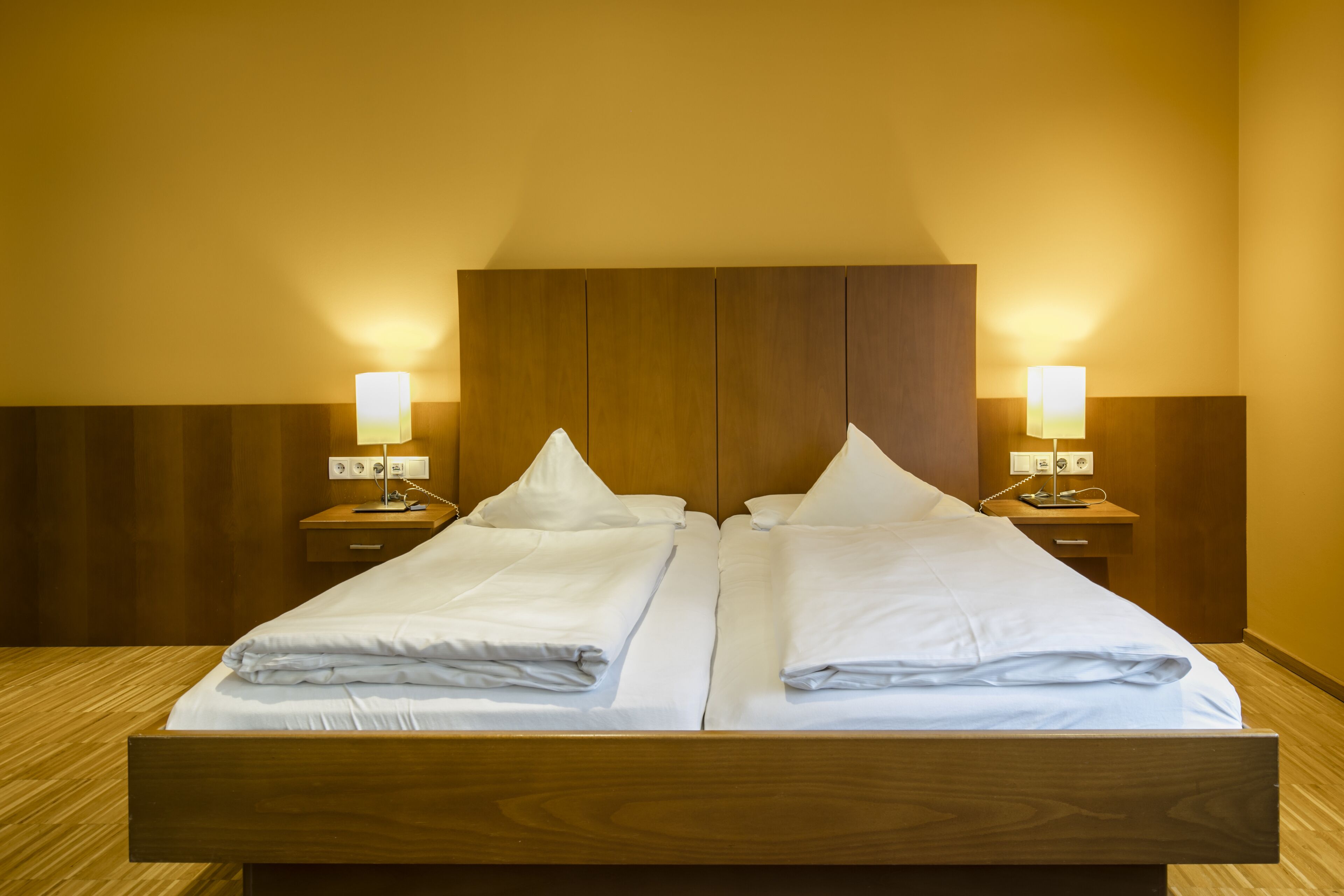 A double bed with two bedside tables, each with a lamp, in a room with wooden paneling and a warm color scheme.