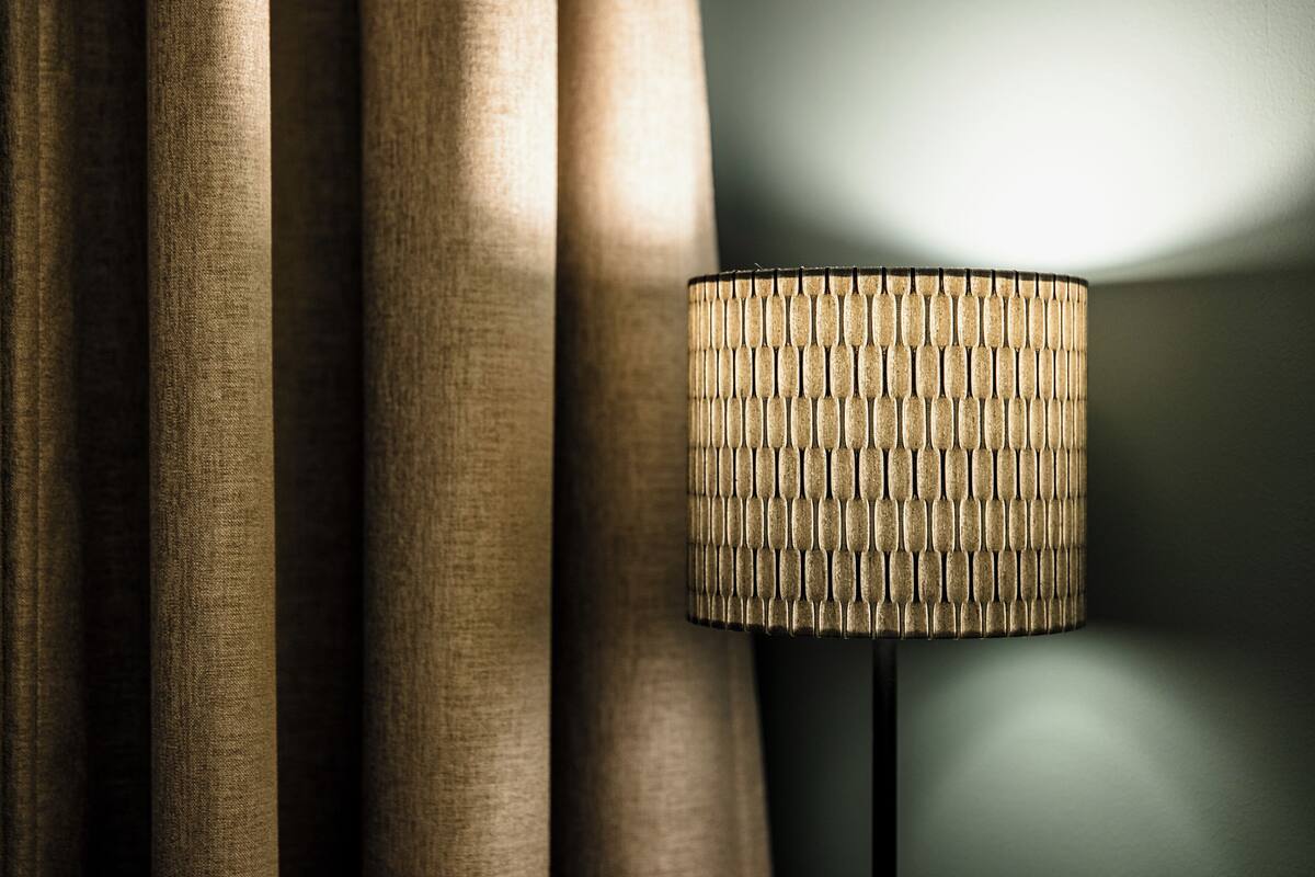 A lamp with a textured shade next to a curtain.