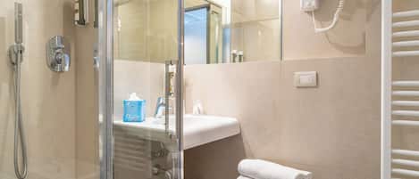 Un baño moderno con cabina de ducha de vidrio, lavabo, espejo, secador de pelo y toallero.