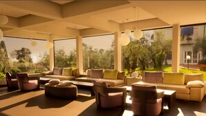 Un salón amplio con un gran sofá, varios sillones y una mesa de centro. Ventanas grandes ofrecen vistas al jardín exterior.