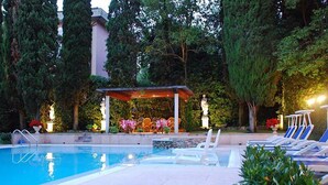Una piscina con sillas de descanso, un área de estar techada con sillas y una estatua.