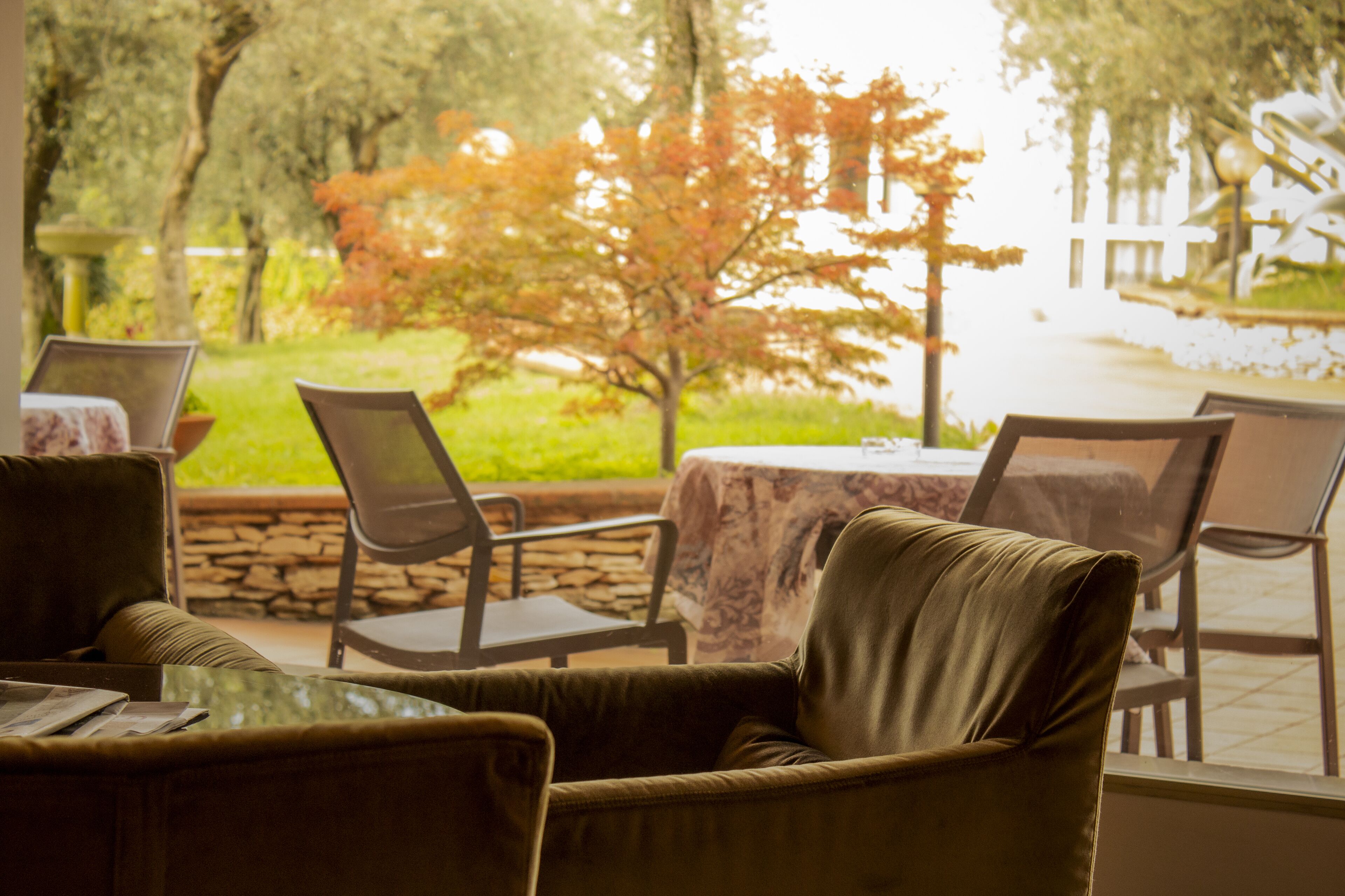 An outdoor seating area with chairs and tables, a stone wall, and a view of trees and a pathway.
