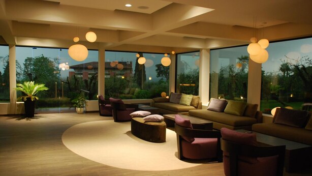 Una sala de estar moderna con un sofá grande, varias sillas y una mesa de centro. Amplias ventanas ofrecen vistas al exterior.