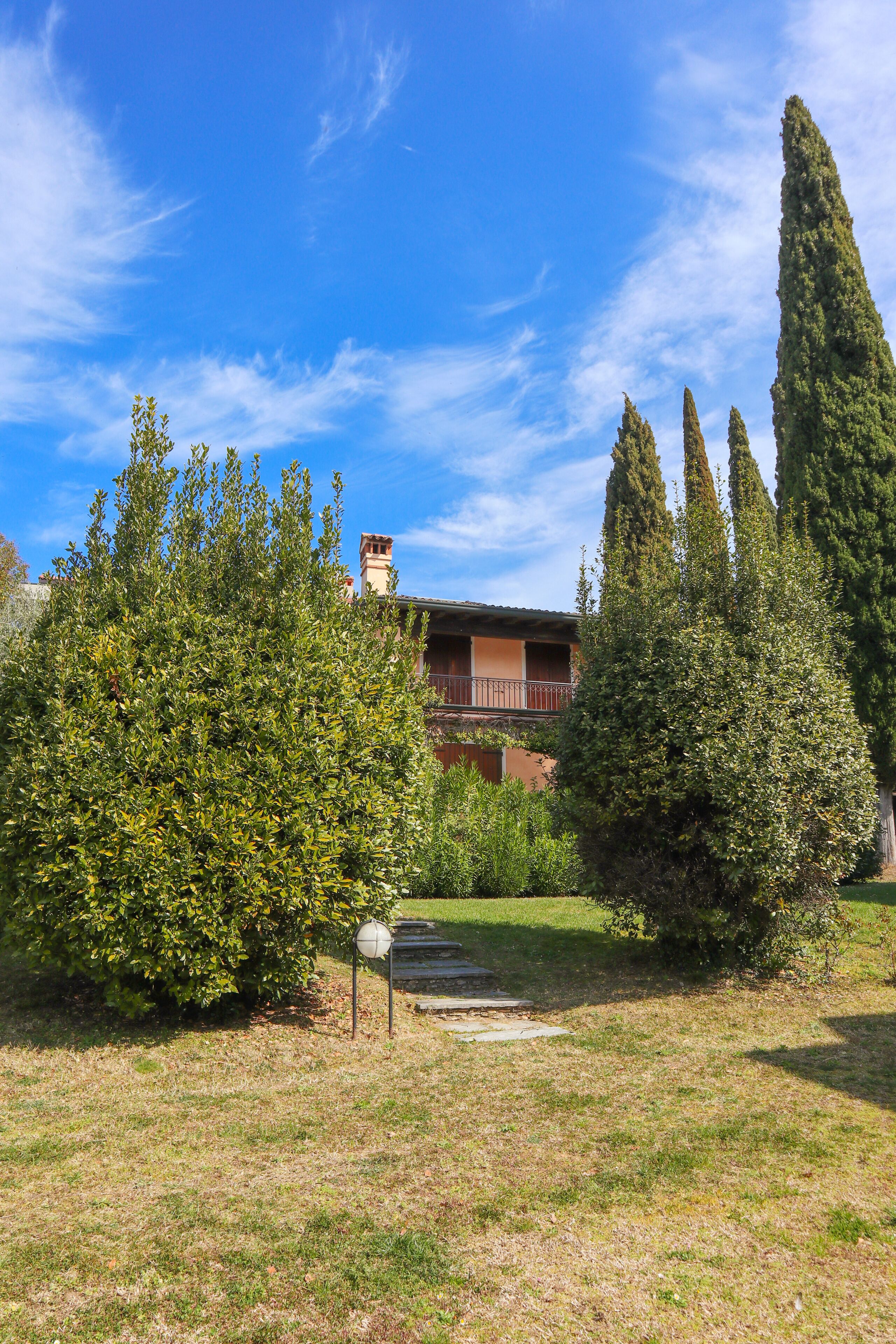 A building with a red roof and a balcony, surrounded by well-maintained greenery and a clear blue sky.
