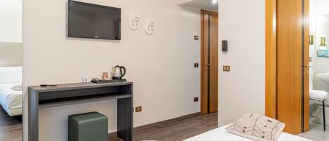 Habitación de hotel con una cama, un escritorio con hervidor, una televisión y una puerta de madera.